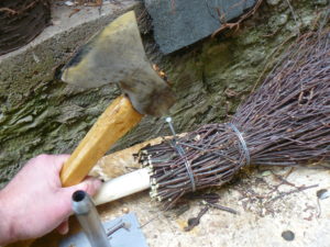 Hammering in nail to hold twig bundle to handle